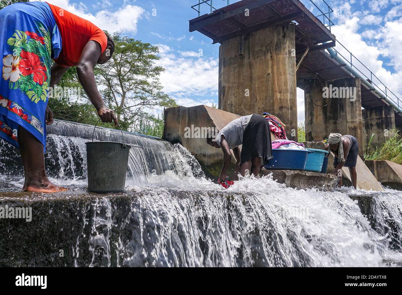Yvonne Kwaedza (from left), Grace Chikata and Rudo Moyana wash their dishes and clothes under a bridge at the Mazowe River near Glendale, Zimbabwe. Stock Photo