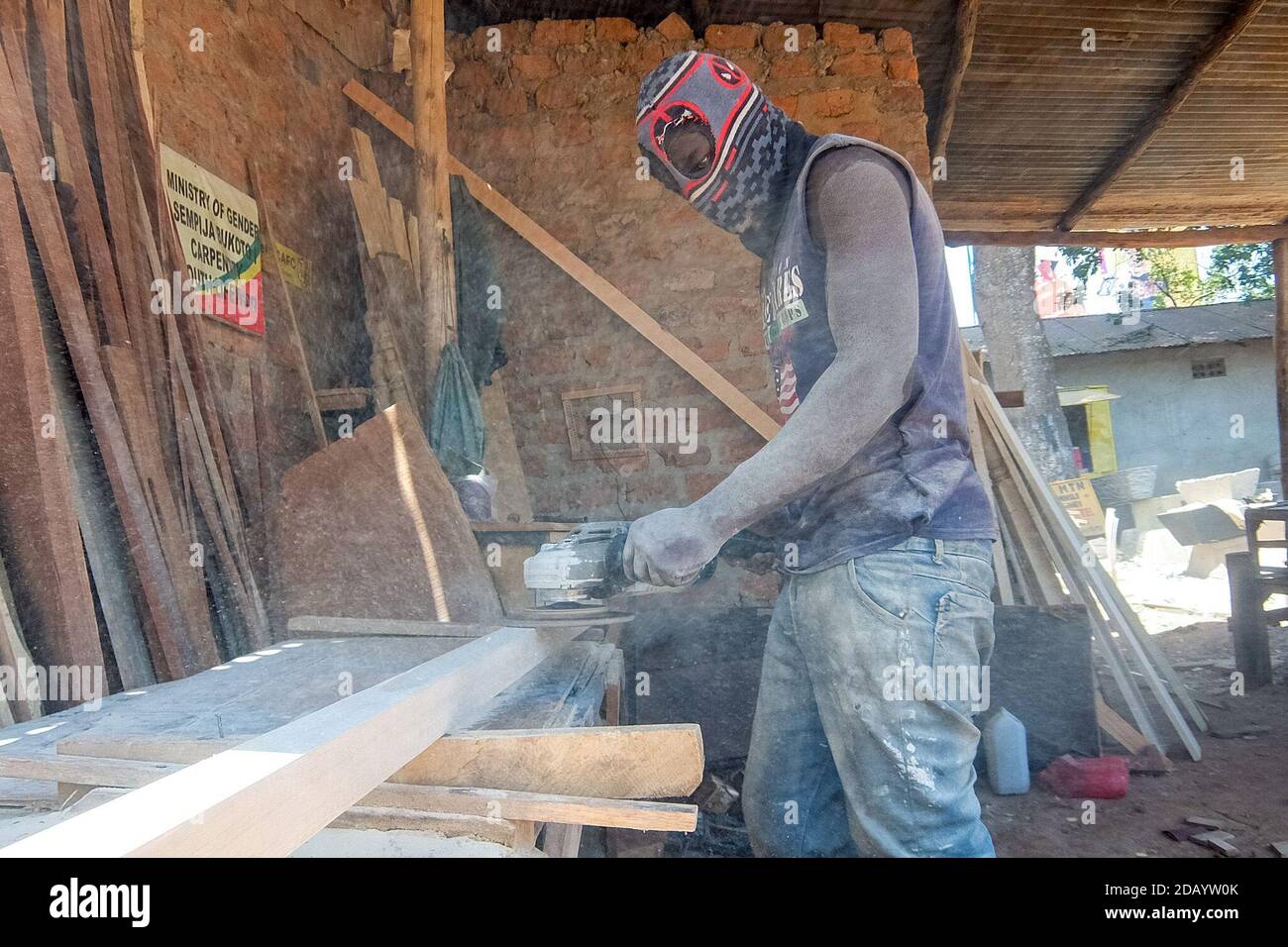 Carpenter Herbert Mubiru, 26, sands the wood he uses for his furniture business in the Bukoto township of Kampala, Uganda. Stock Photo