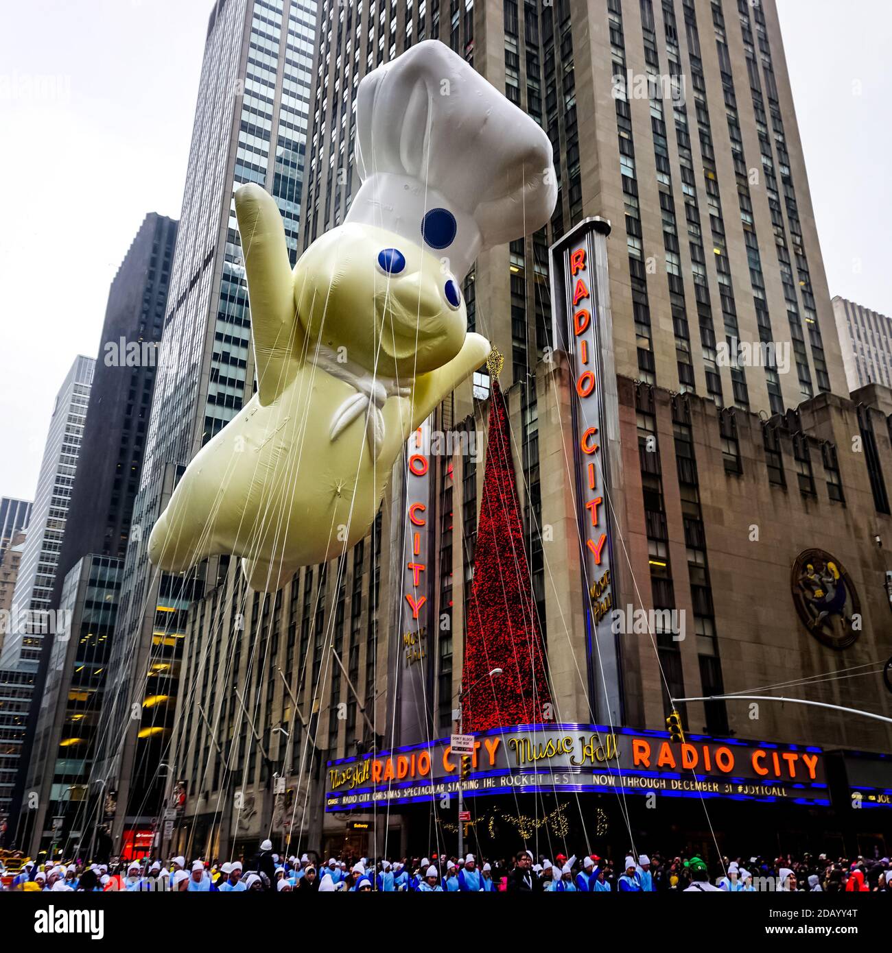 The Pillsbury Doughboy balloon floats in the air during Macy's Thanksgiving Day parade along Avenue of Americas with Radio Music Hall in background. Stock Photo