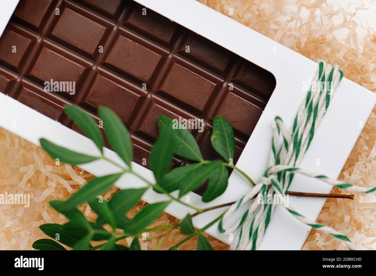 Chocolate bar in a white windowed box, tied with a rope. Plant branch attached. Stock Photo