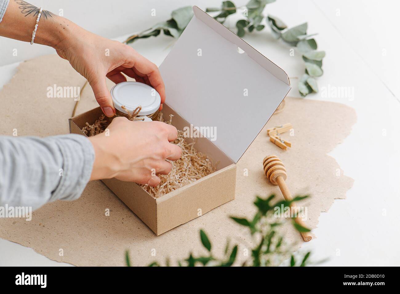 Hands carefully placing small jar with honey in a box with filling