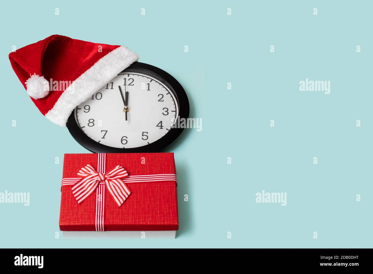 Christmas composition with a classic analog clock in a red Christmas cap and a red gift box isolated on a gentle blue background, top view, placed on Stock Photo