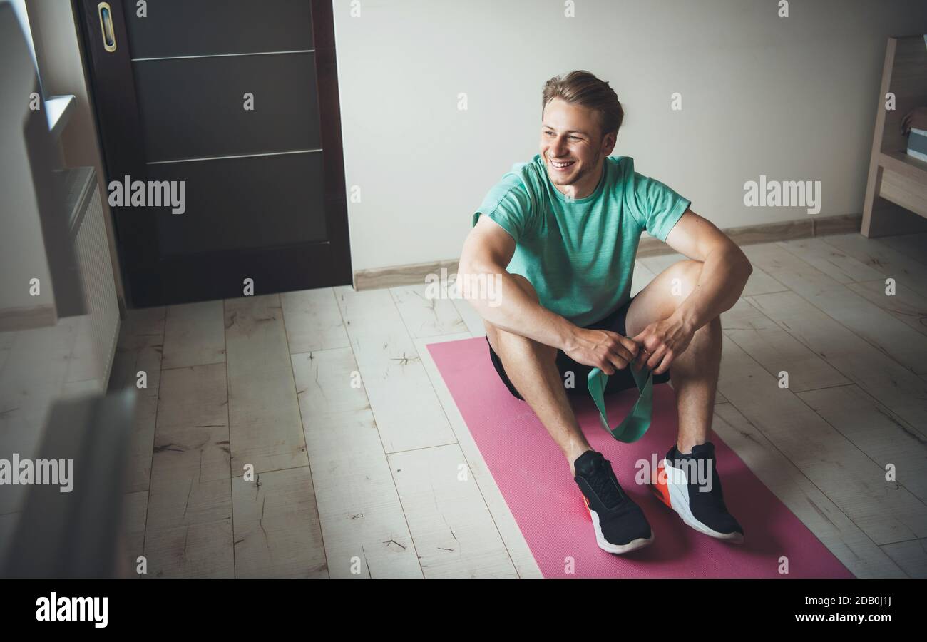 Smiling man with blonde hair wearing sportswear on the floor during a fitness lesson at home Stock Photo