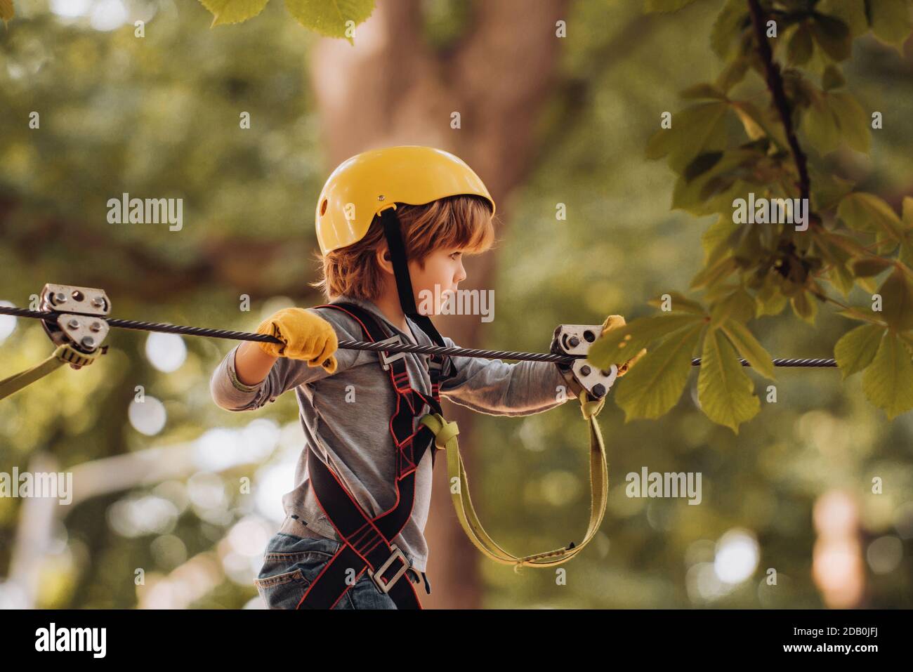 Happy child climbing in the trees. Children summer activities. Early childhood development. Child. Safe Climbing extreme sport with helmet Stock Photo