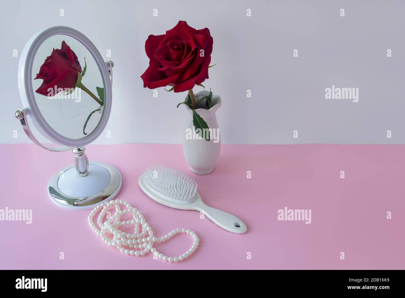 Red rose in white vase on table with hairbrush and pearls. Wedding preparation concept. Selective focus, blur. Stock Photo
