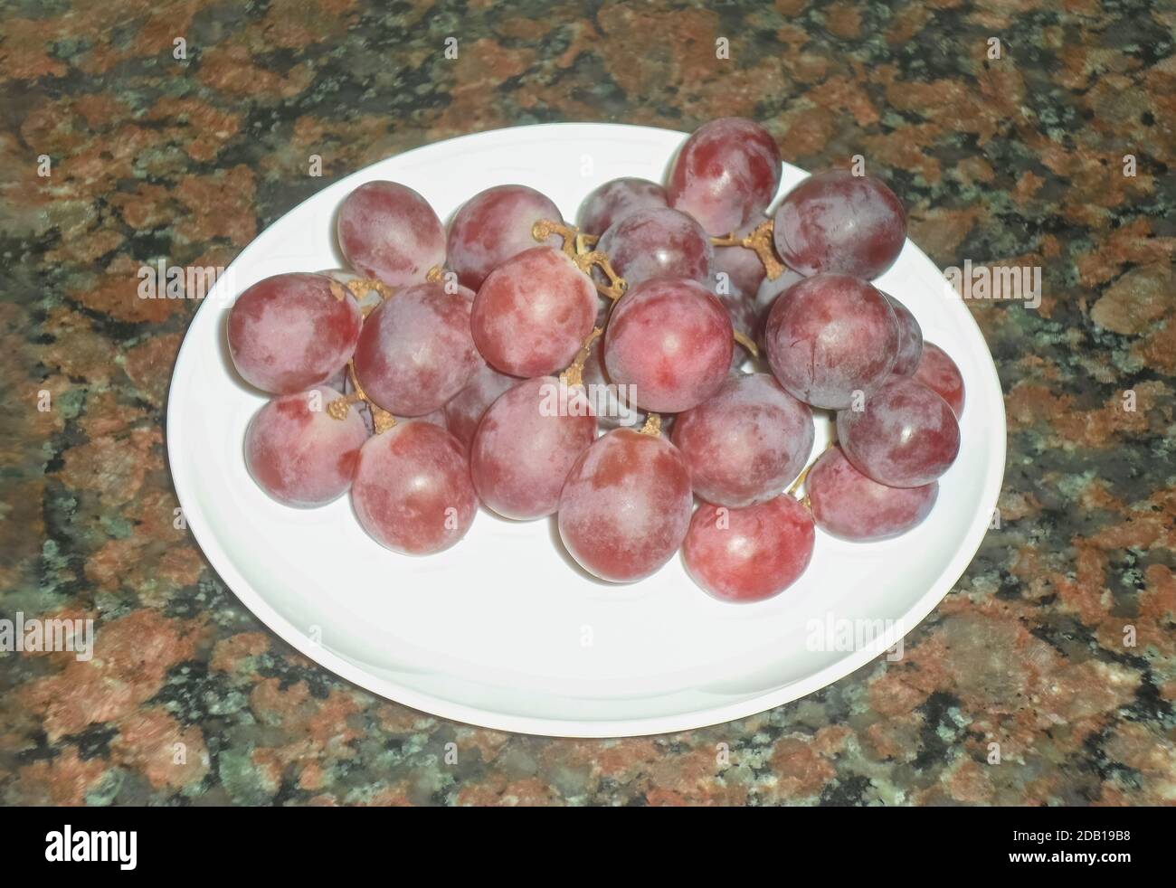 High angle view of a bunch of fresh sweet ripe red grapes in a plate on a marble background Stock Photo