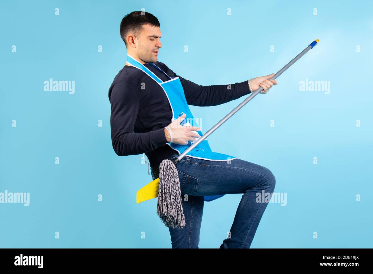 Cheerful man in an apron, having fun and dancing with a mop while
