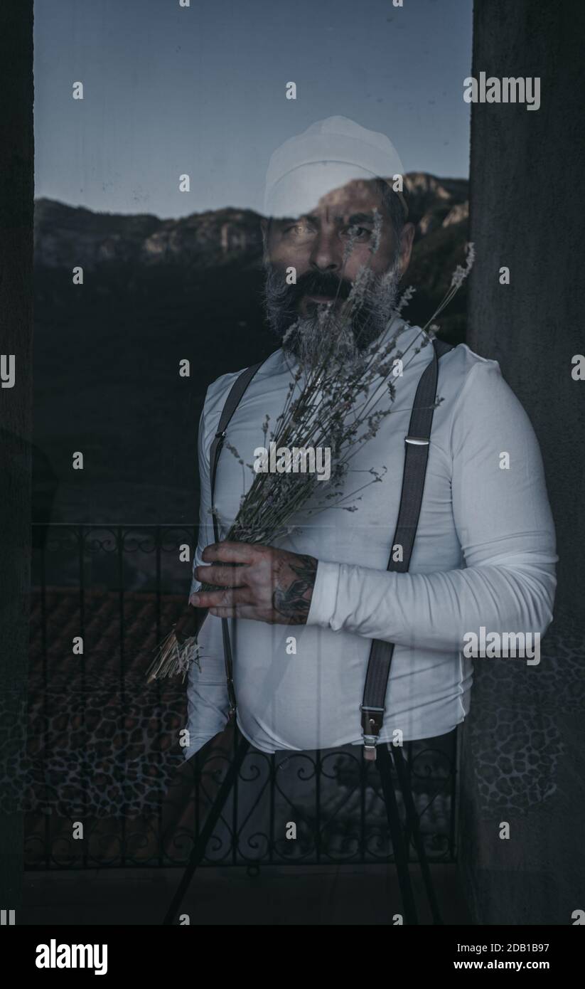Portrait bearded man looking out window in dark room Stock Photo