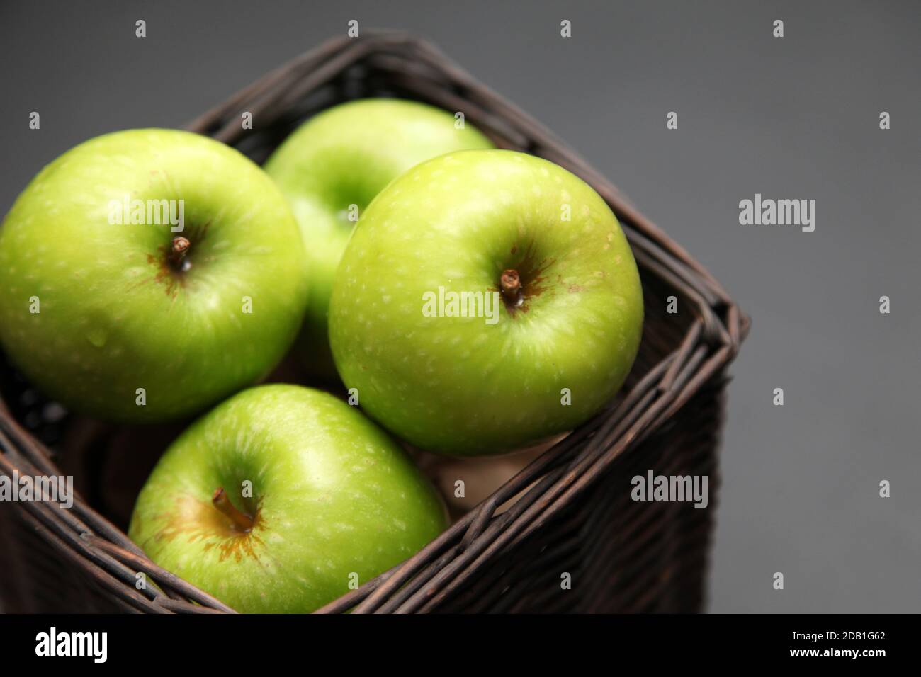 Five green apples in a basket on a dark background Stock Photo