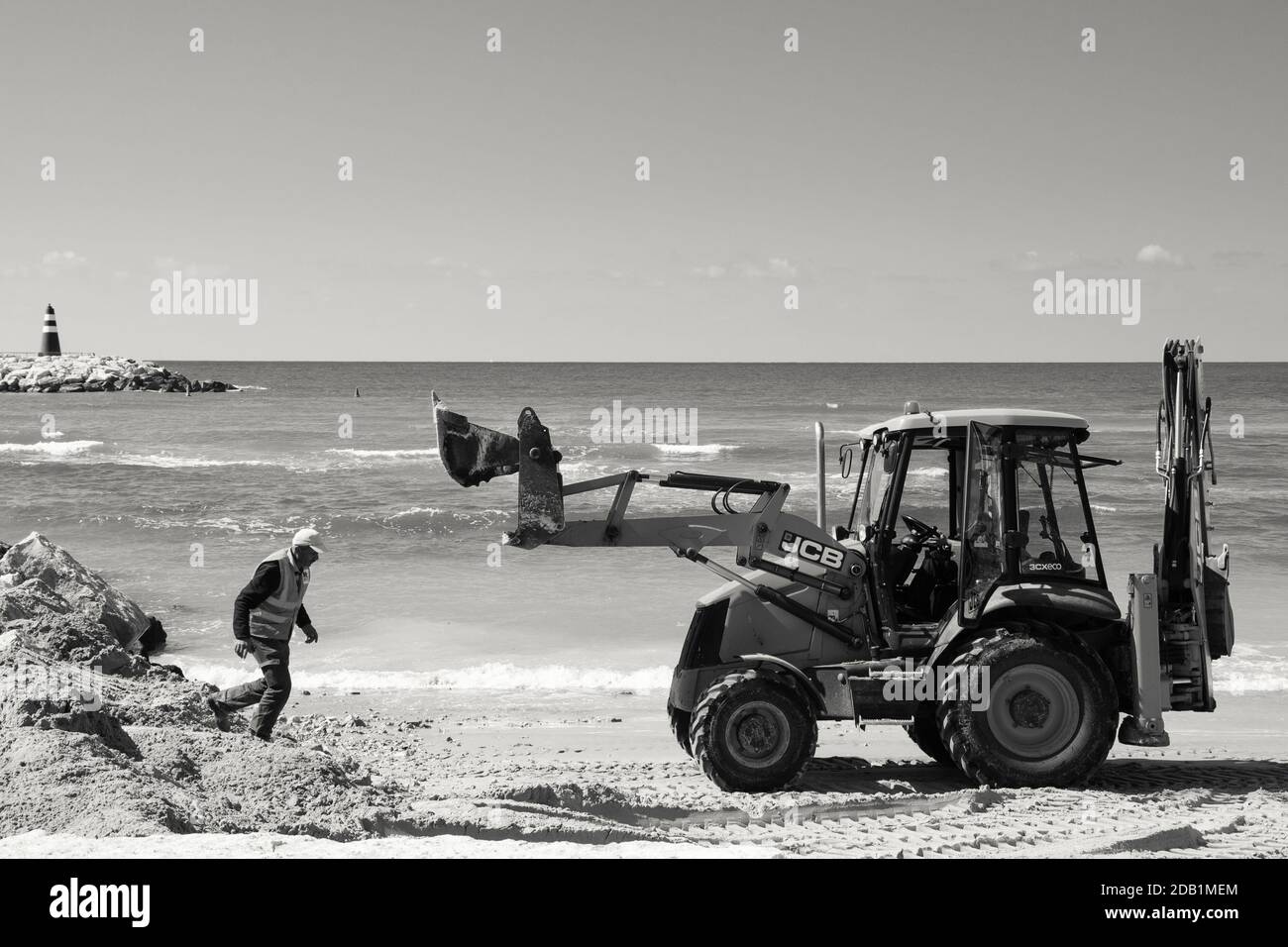 TEL AVIV, ISRAEL - MARCH 6, 2019: Beach industrial scene. Workers making repairs at the beach with digger. Black white photo Stock Photo