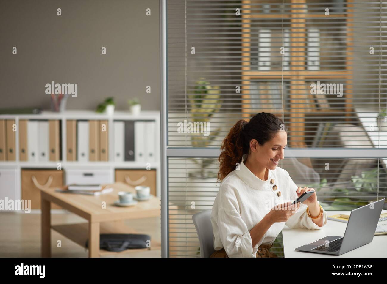 High angle portrait of elegant successful businesswoman using smartphone and smiling while enjoying work from home, copy space Stock Photo
