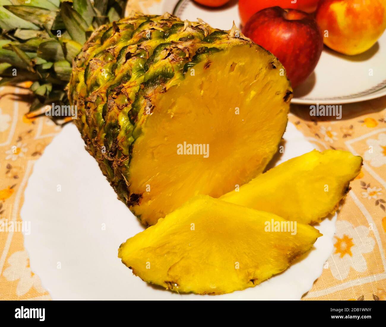 Pineapple fruit on white plate and red apples in the background Stock Photo