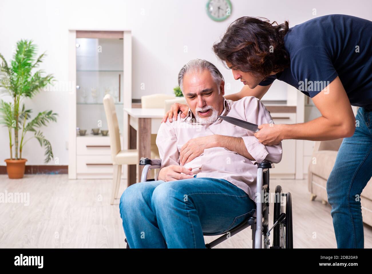 Old man in wheel-chair and bad caregiver indoors Stock Photo