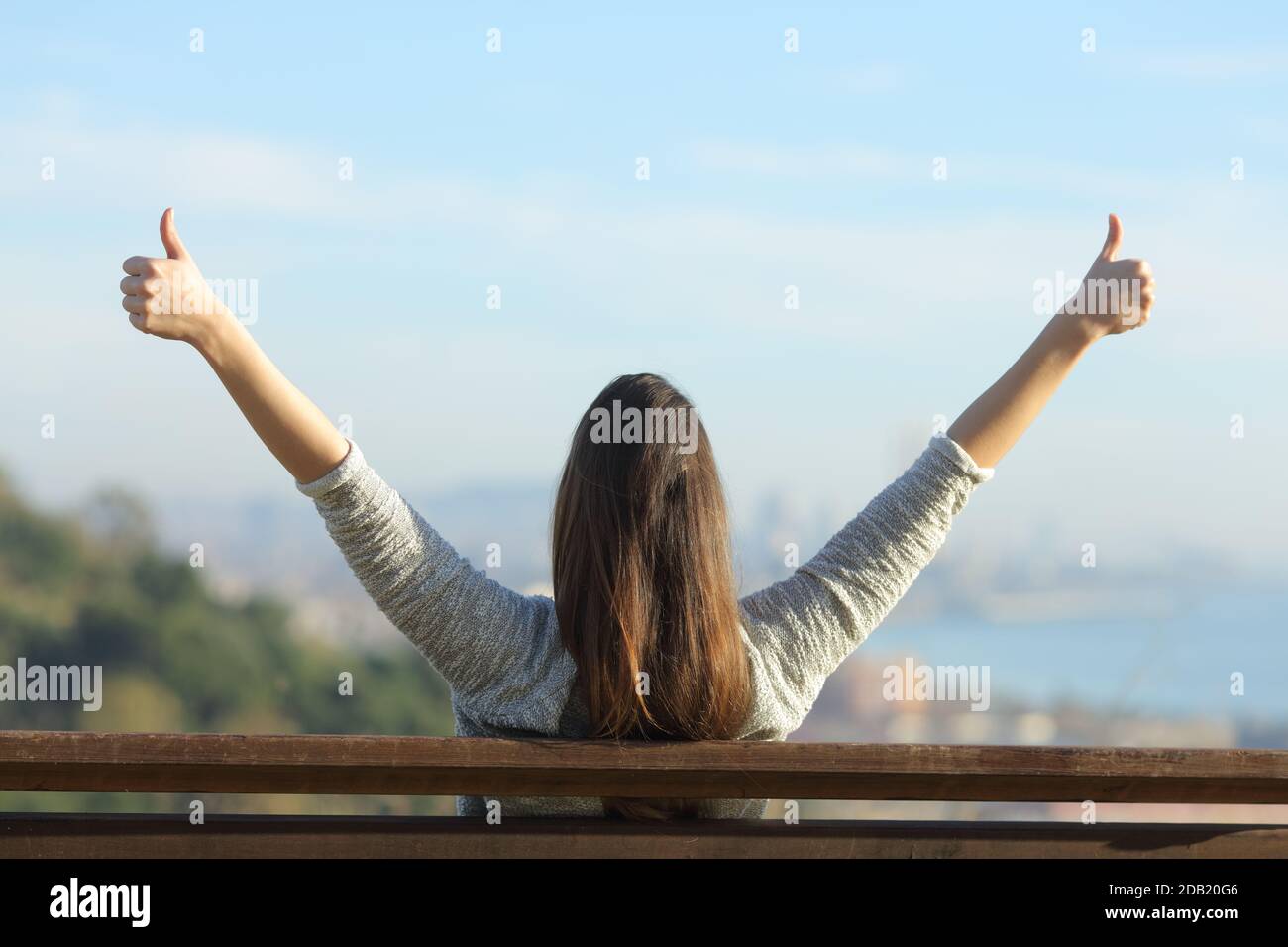 Back view portrait of a happy woman raising hands with thumbs up ...
