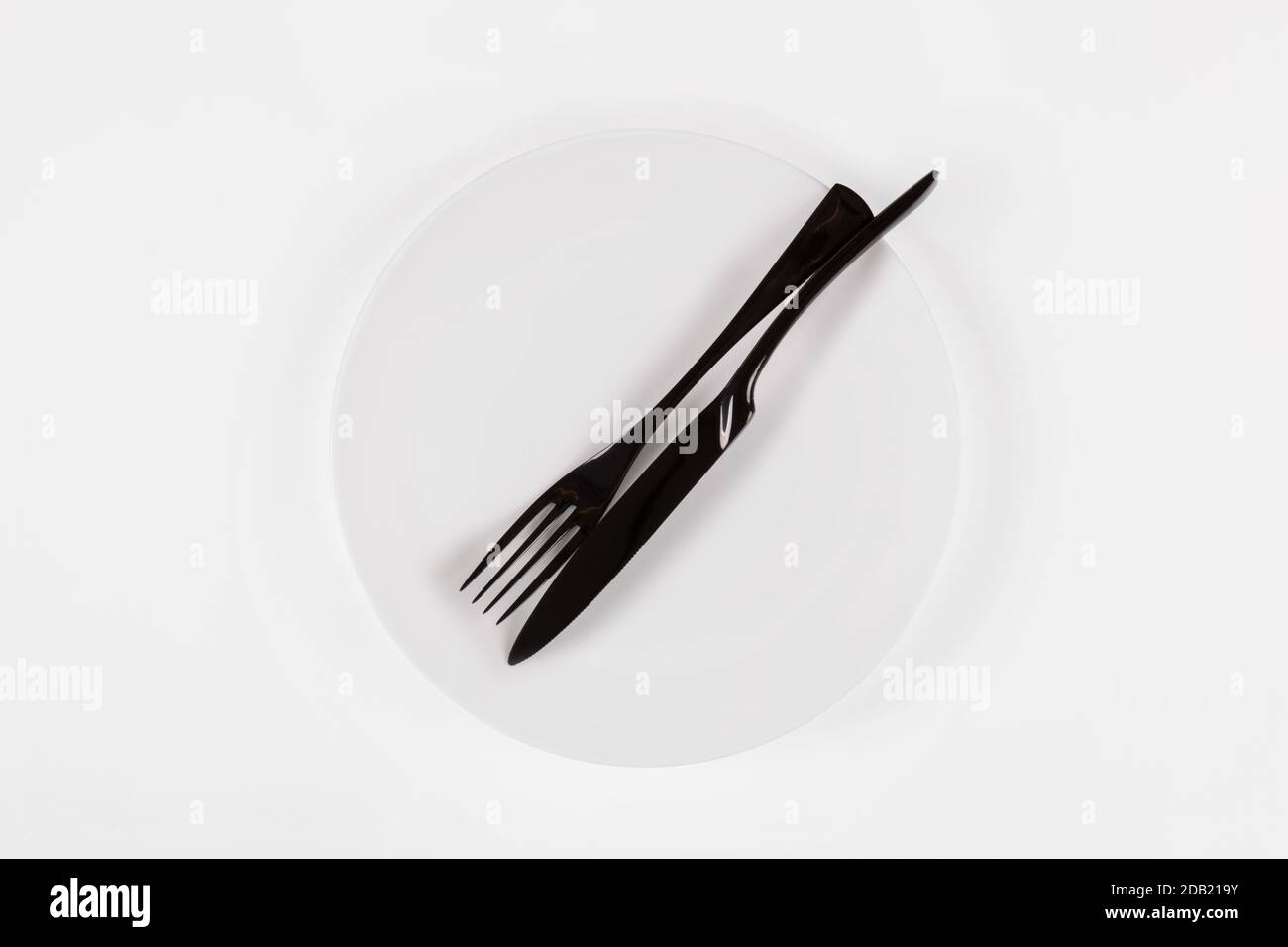 Cutlery language, dining etiquette. The meal is over. White ceramic round plate with knife anf fork isolated on white, top view. Stock Photo