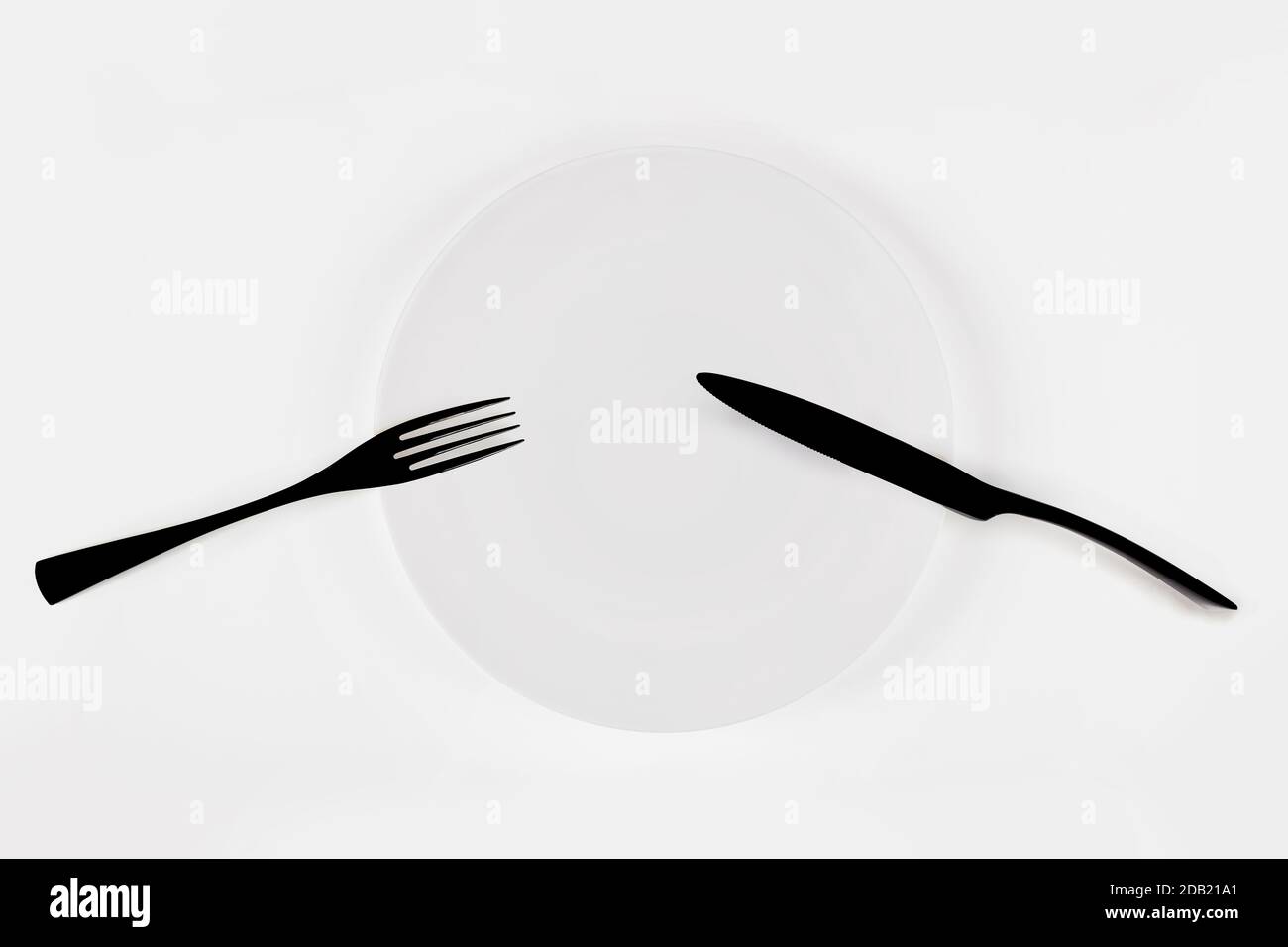 Cutlery language, dining etiquette. Pause. White ceramic round plate with knife anf fork isolated on white, top view. Stock Photo