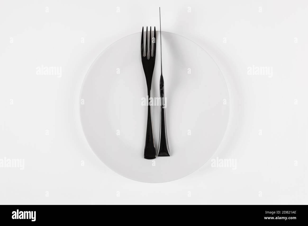 Cutlery language, dining etiquette. Excellent food. White ceramic round plate with knife anf fork isolated on white, top view. Stock Photo
