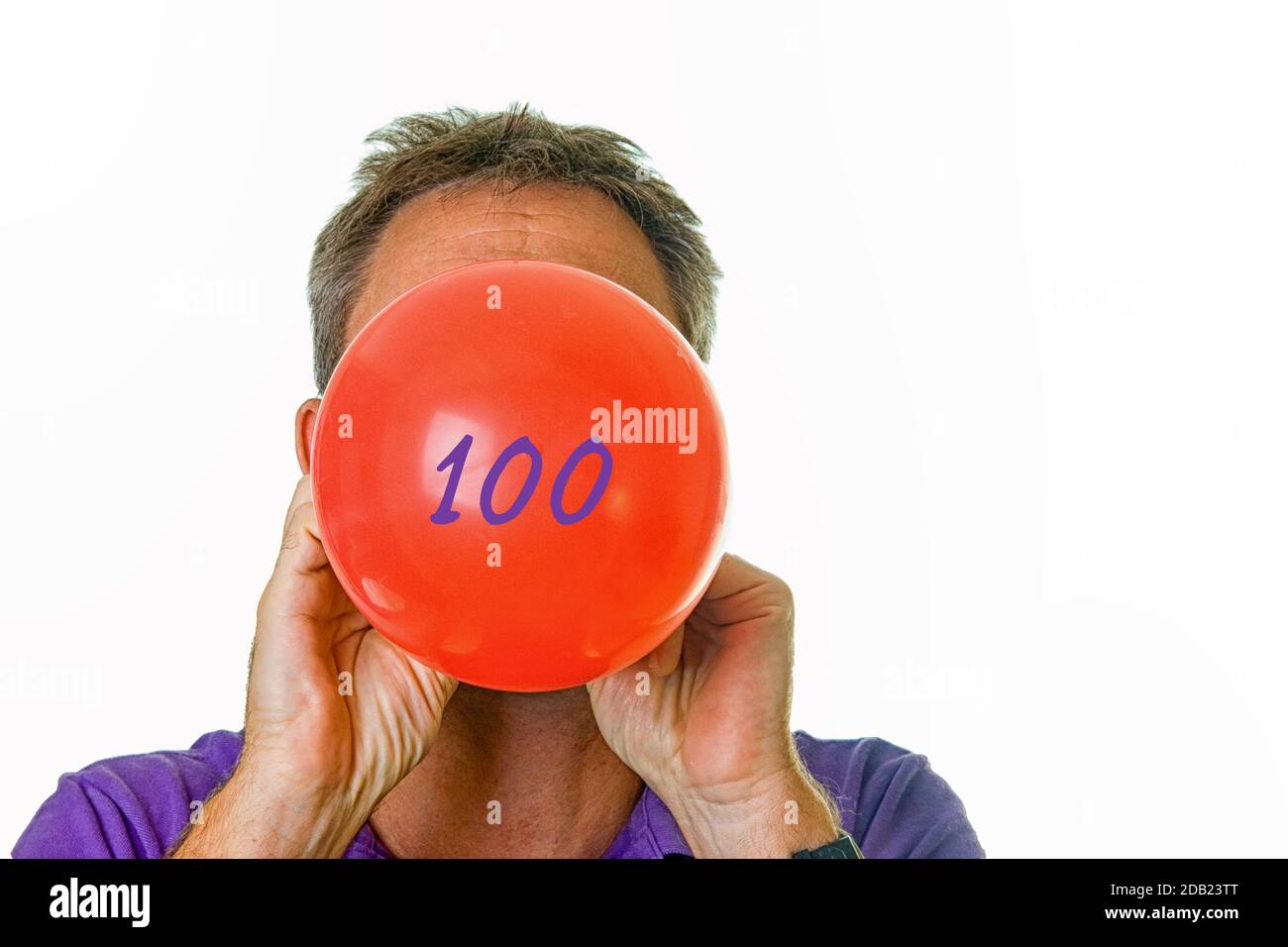 Man blowing red balloon with number 100 Stock Photo