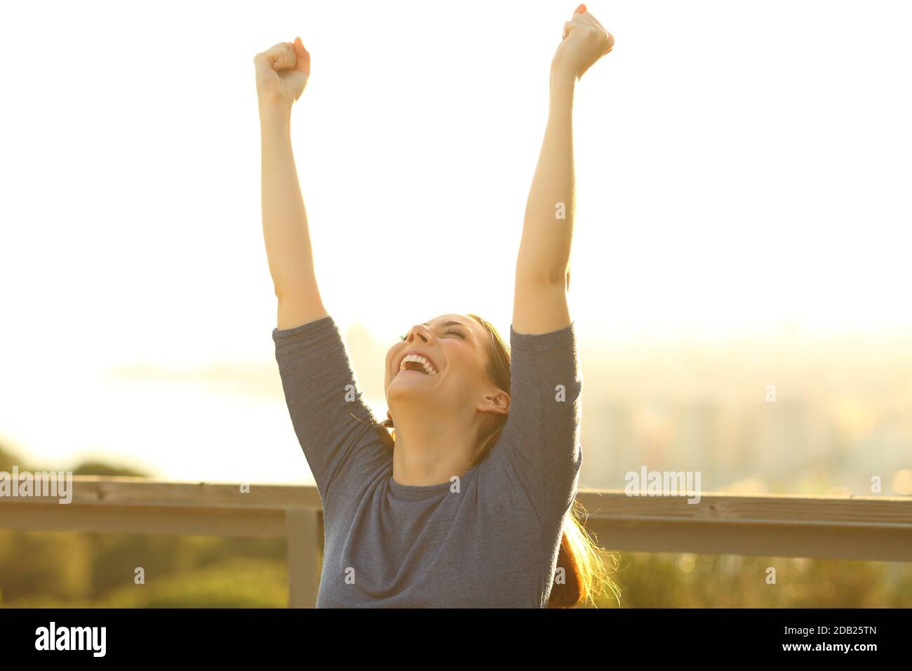 Excited woman raising arms celebrating success at sunset in a park ...