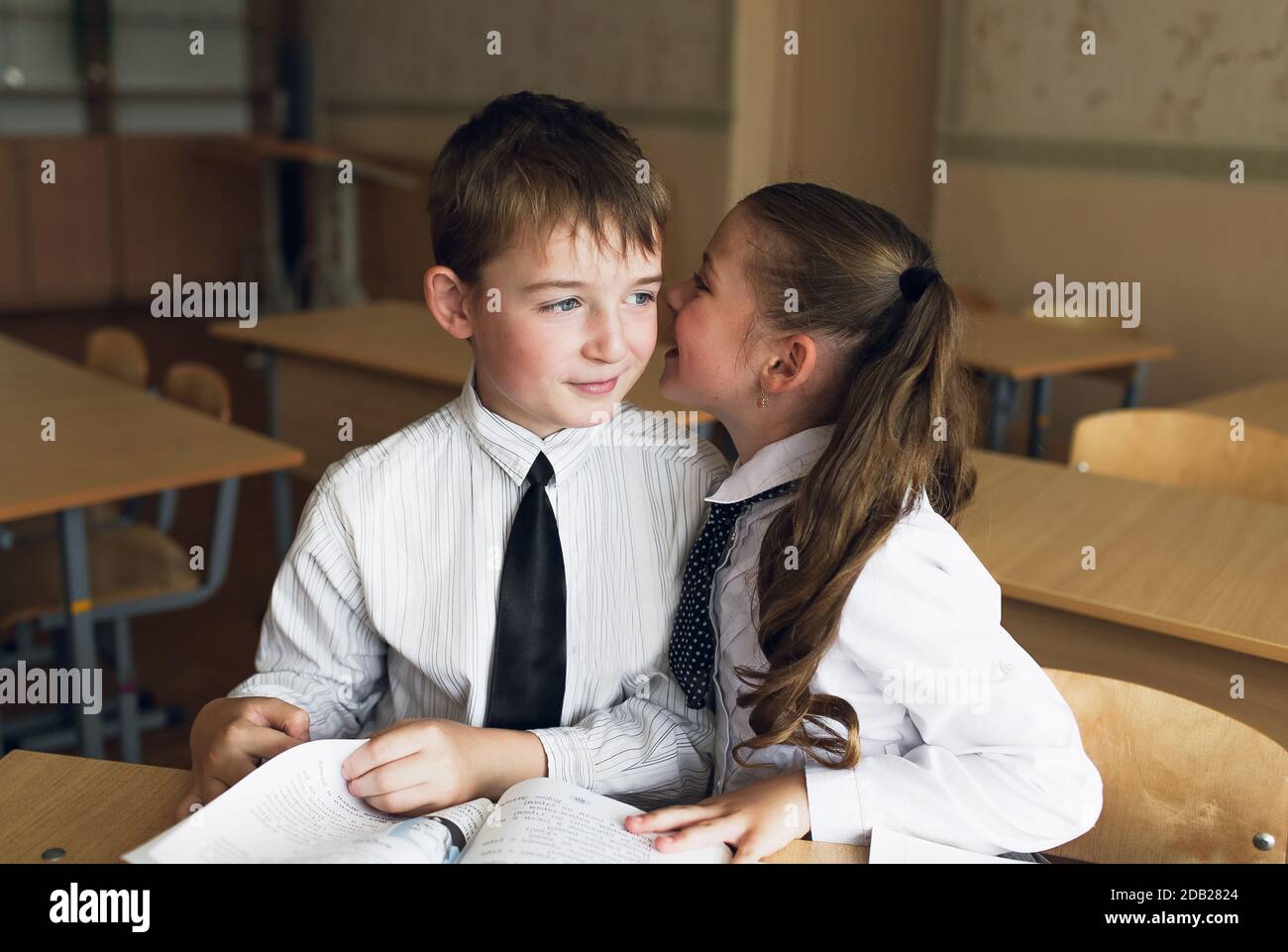 a boy and a girl students sit at a Desk and talk in each other's ear Stock Photo