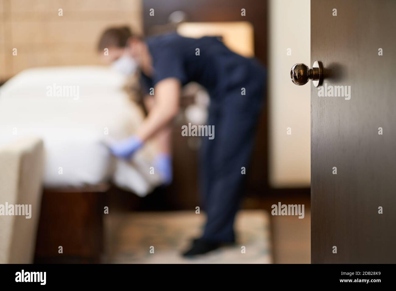 Wooden door to hotel room with maid during cleaning in the background. Hotel service concept Stock Photo