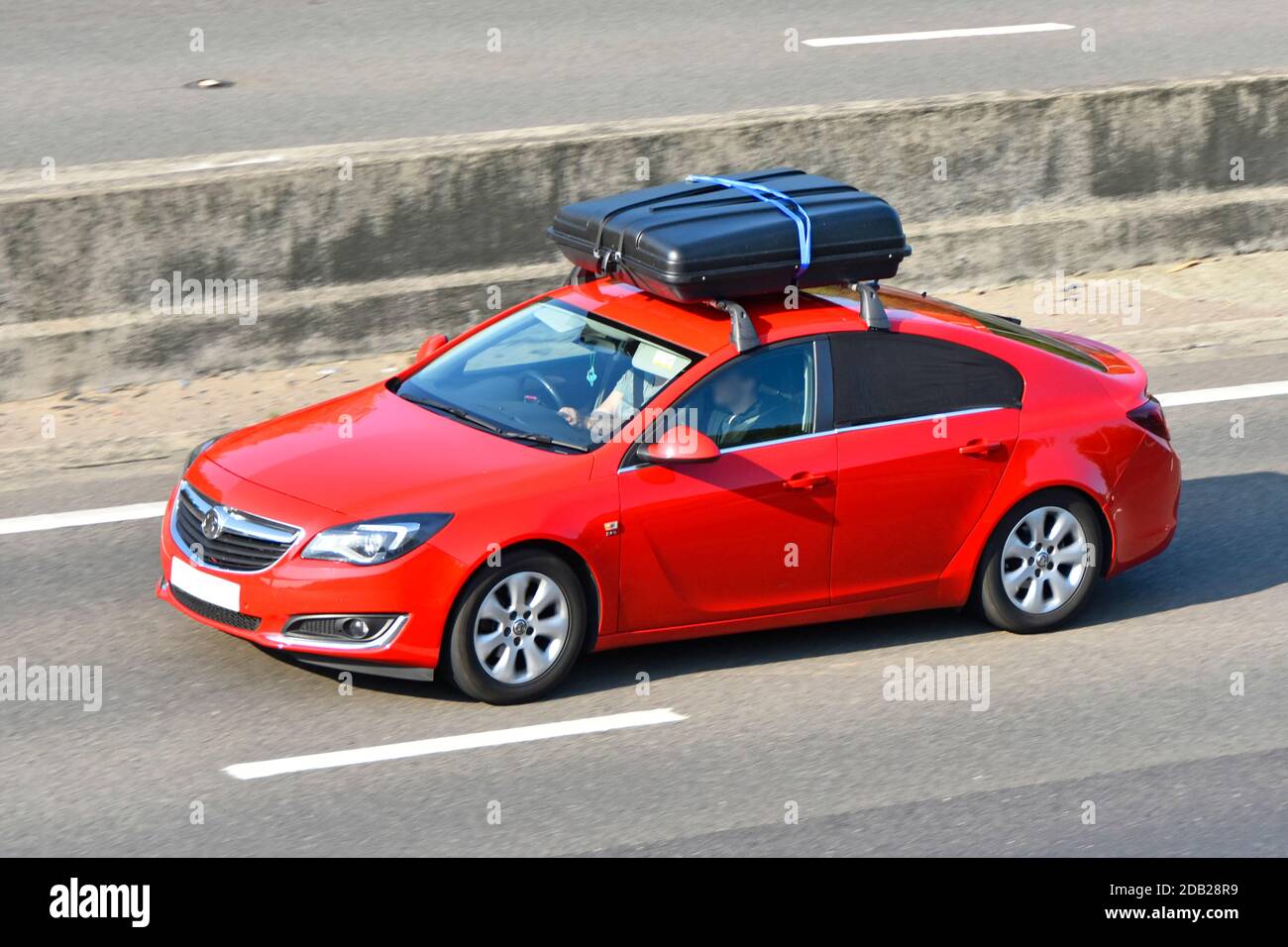 Aerial front & side view a red hatchback car driver & front seat passenger roof rack & black luggage box insitu concrete UK motorway crash barrier Stock Photo