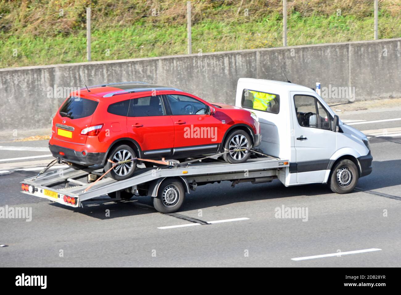 Unmarked white vehicle breakdown or trade delivery pick up car transporter truck van transporting red Nissan qashqai ntec load driving on UK motorway Stock Photo