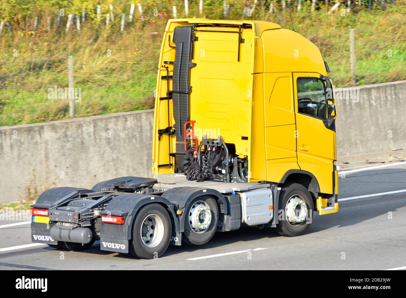 Back & side view cab of yellow clean Volvo solo semi truck tractor unit prime mover twin rear axle lorry with one axle raised & exhaust on UK motorway Stock Photo