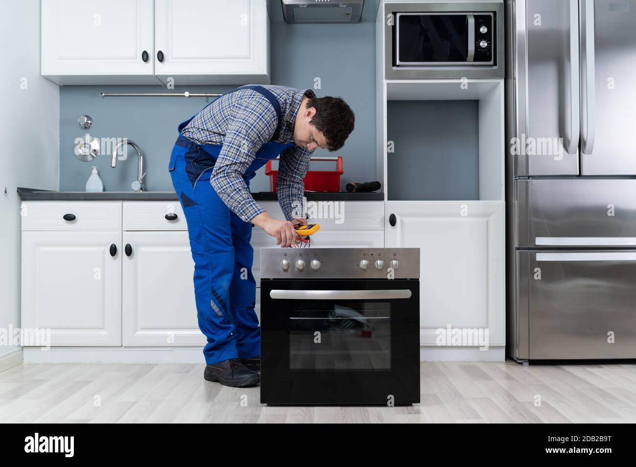 Young Male Technician Checking Oven With Digital Multimeter Stock Photo