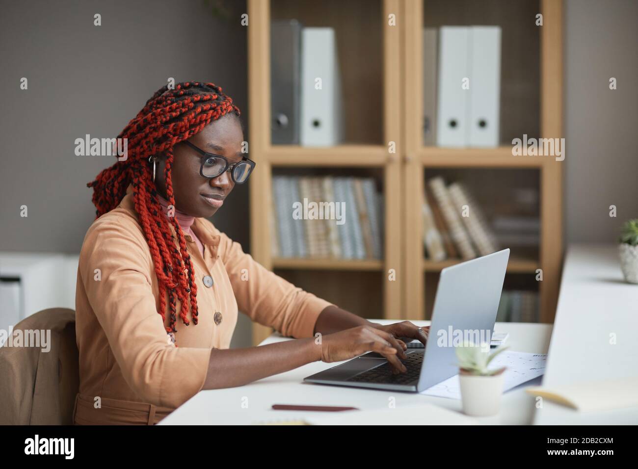 Side view portrait of young African-American woman using laptop while studying or working from home at workplace, copy space Stock Photo