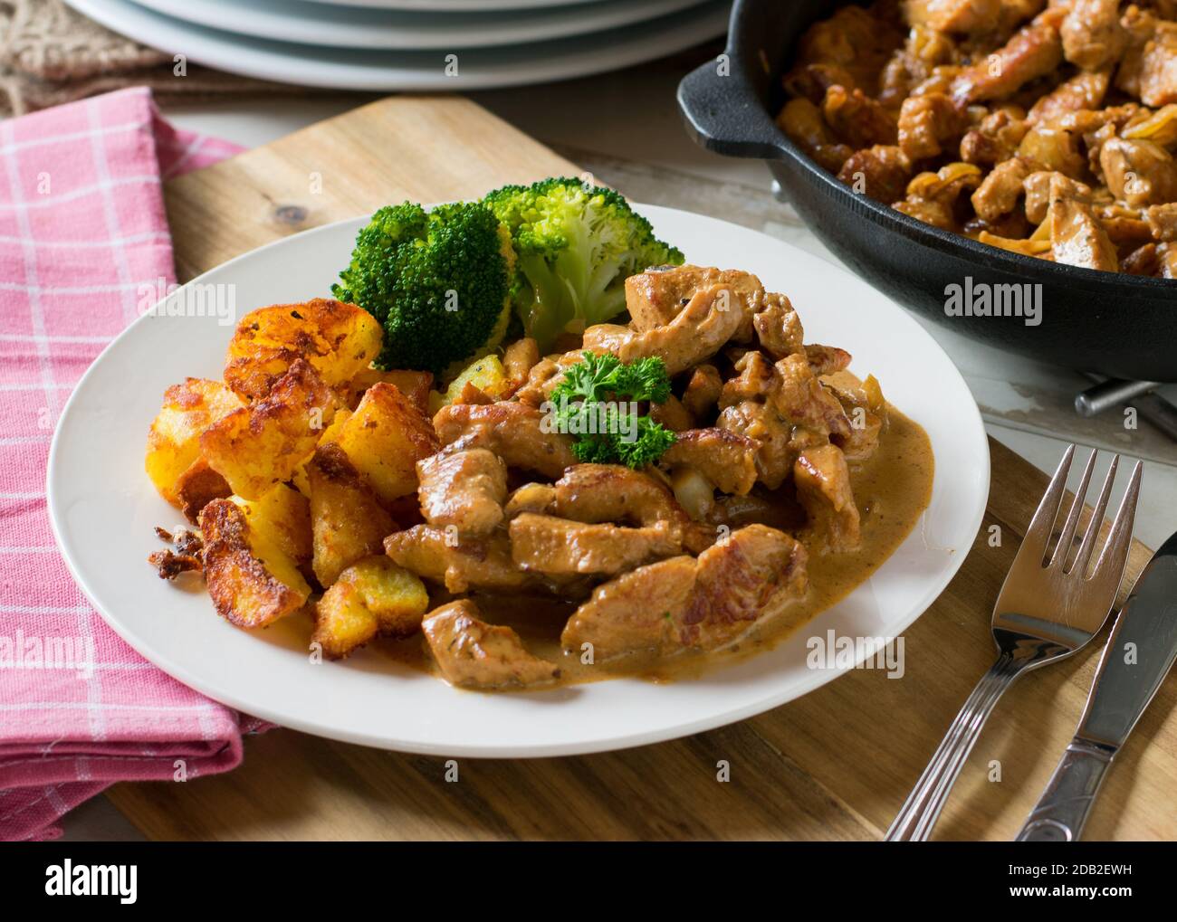 sauteed pork meat with cream sauce, fried potatoes and vegetables on a
