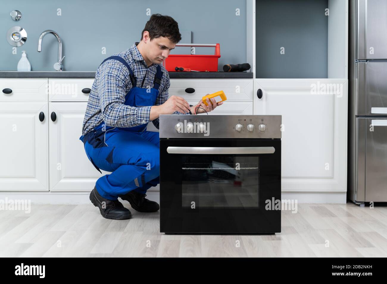 Young Male Technician Checking Oven With Digital Multimeter Stock Photo