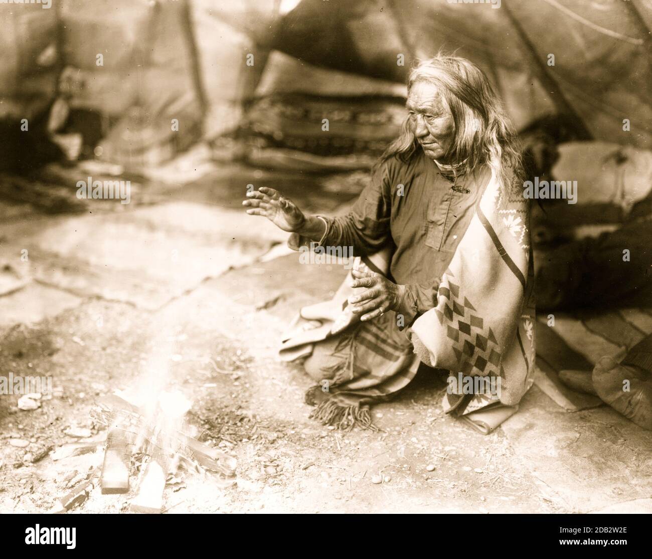 Navajo Indian warming hands over fire in tepee.. Stock Photo