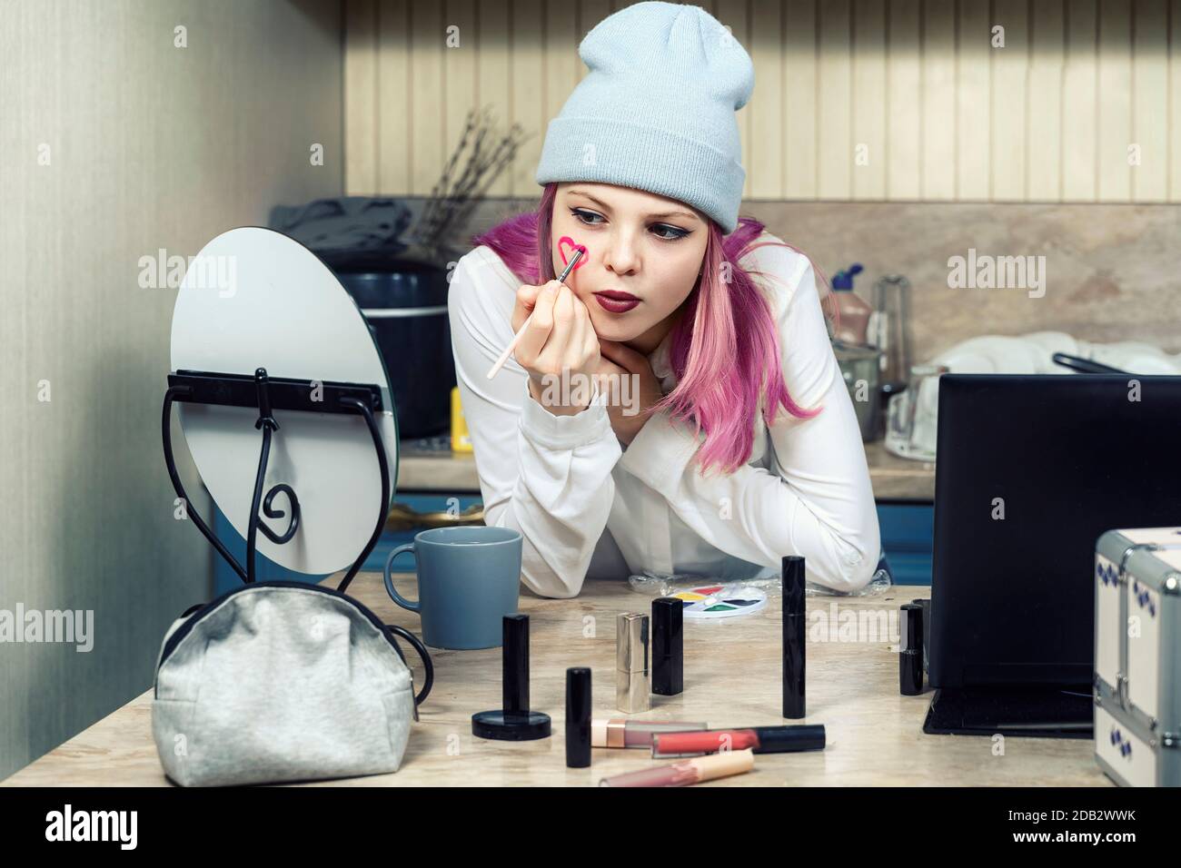 girl teenager with pink hair makes bright makeup at home in front of the mirror. adolescents and subculture. Stock Photo
