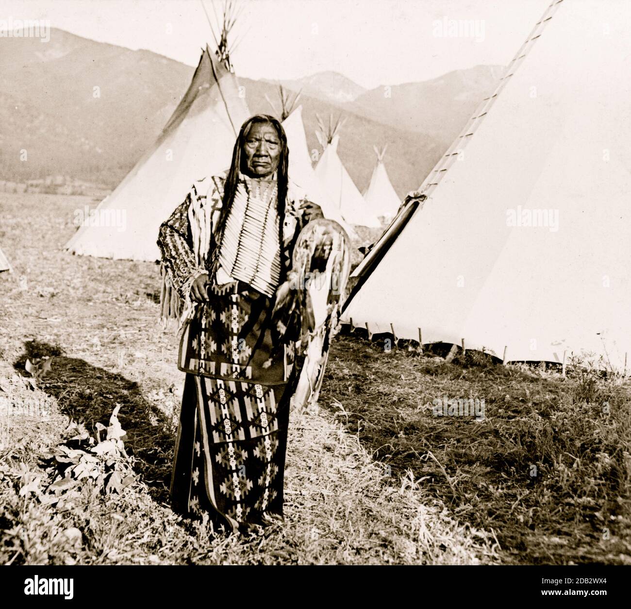 Chief Charlot, full-length portrait, standing, facing front, with tipis behind him, Flathead Reservation, Montana.. Stock Photo
