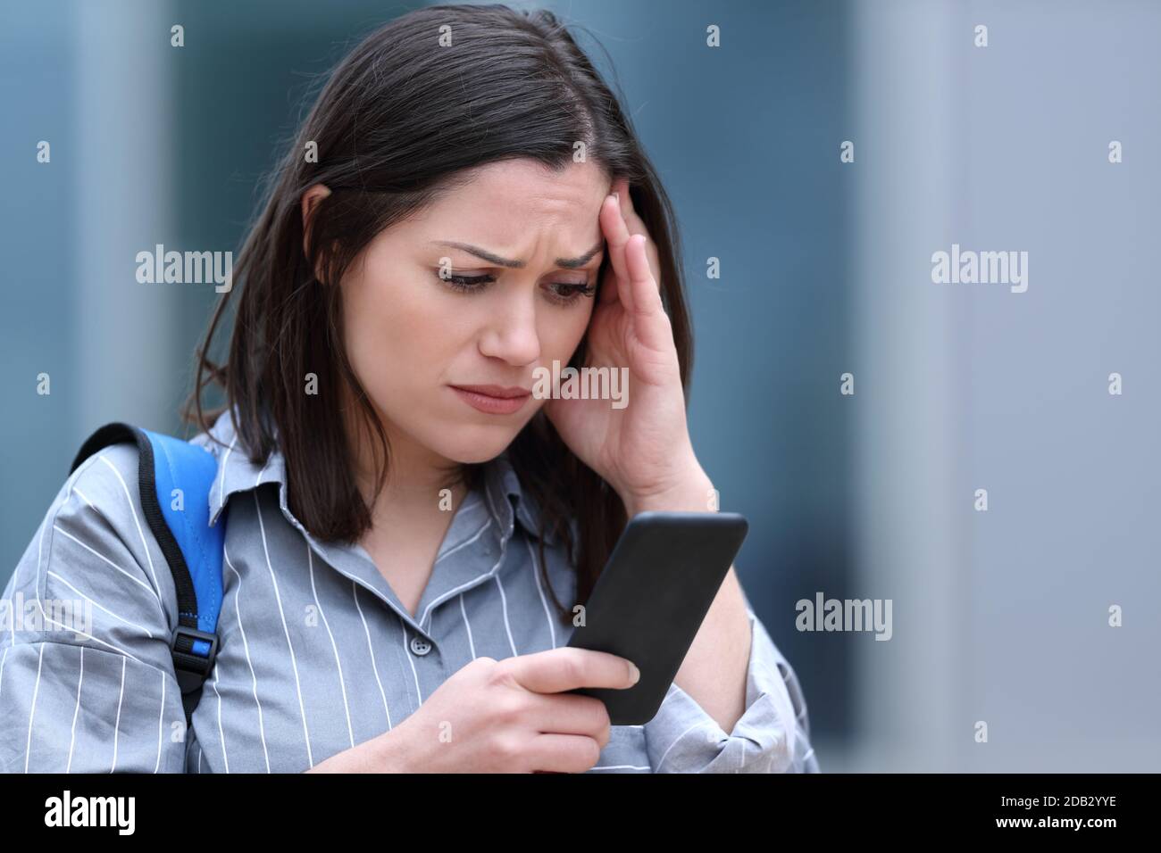 Worried student checks smart phone message walking in the street Stock Photo
