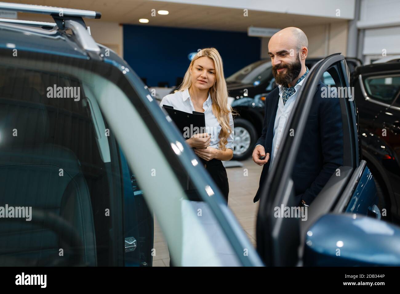 Smiling man and saleswoman in car dealership. Customer and seller in vehicle showroom, male person buying transport, auto dealer business Stock Photo