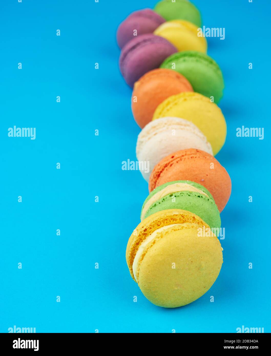 round multi-colored baked macarons with cream lie in a line on a blue ...