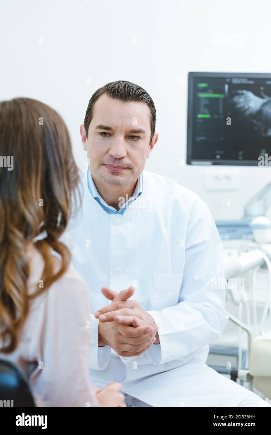 Gynecologist in his doctors office seeing a patient explaining her she