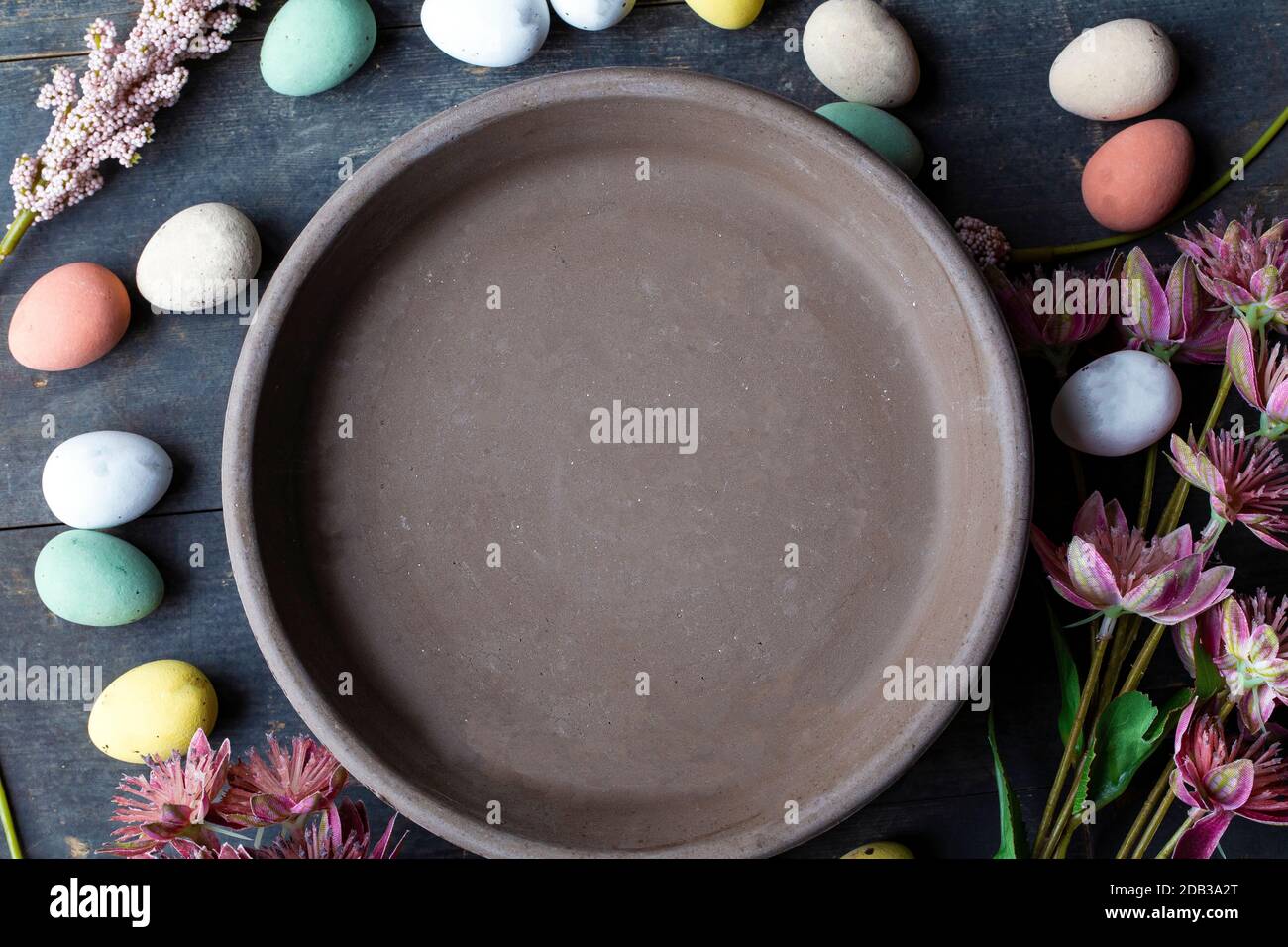 Grey Ceramic Plate with painted Easter Eggs of pastel colors on vintage wooden background. Happy Easter card concept, minimalistic design, top view Stock Photo