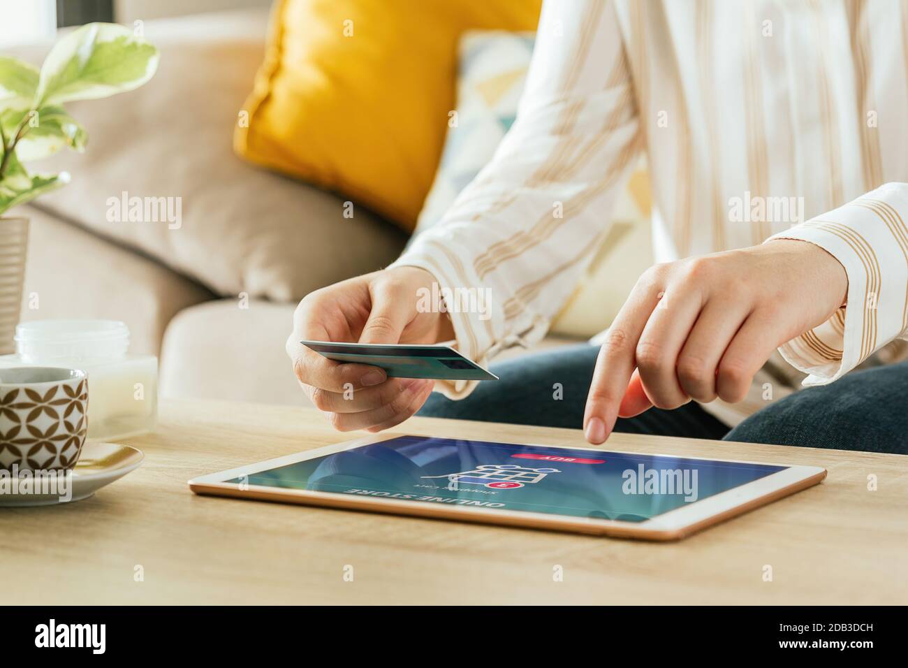 Stock photo of an unrecognizable woman paying and order online with the tablet and a credit card from the couch at living room. E-commerce concept Stock Photo