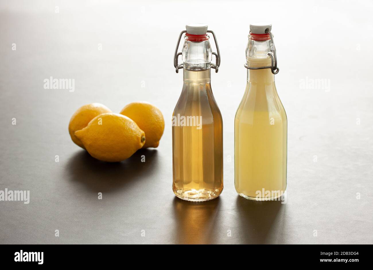 Two flip-top patent closure bottles with homemade lemon syrup or juice and three lemons in background. Partly backlit studio shot image with reflectio Stock Photo