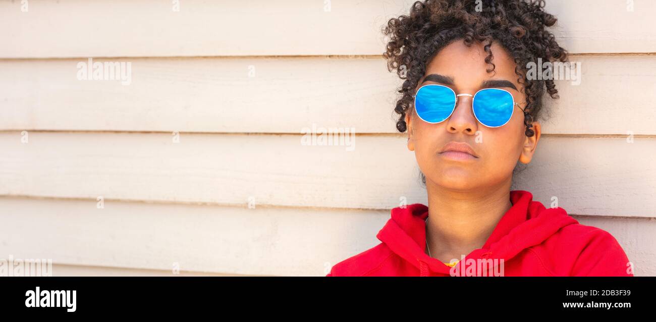 Panorama girl teenager cool teen mixed race biracial African American female young woman wearing blue sunglasses and a red hoodie on summer vacation Stock Photo
