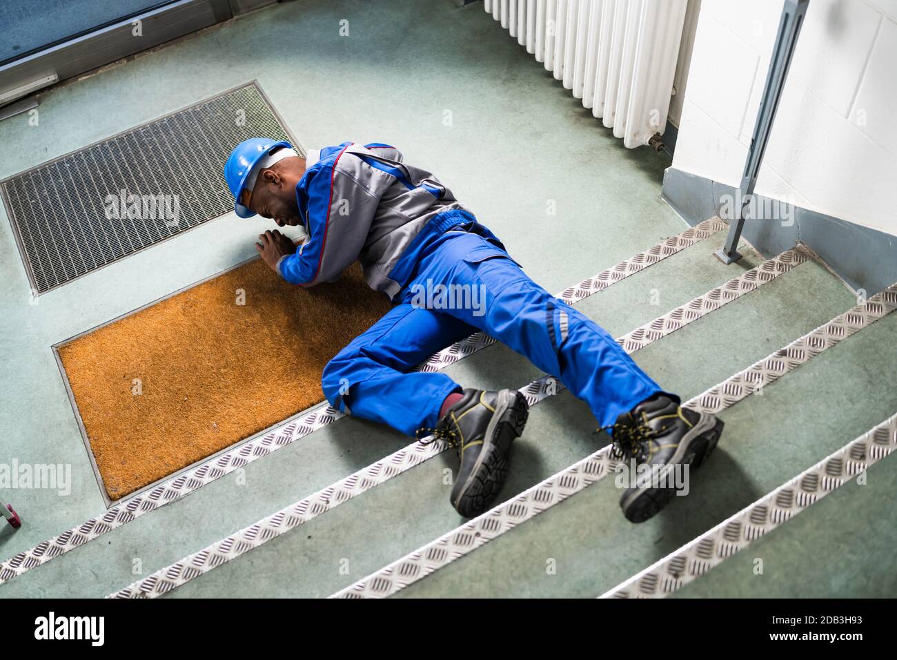 Unconscious Handyman Lying On Staircase With Helmet On Floor Stock Photo