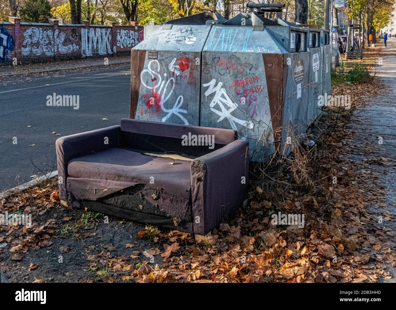 Containers for trash collection and abandoned old sofa on sidewalk in