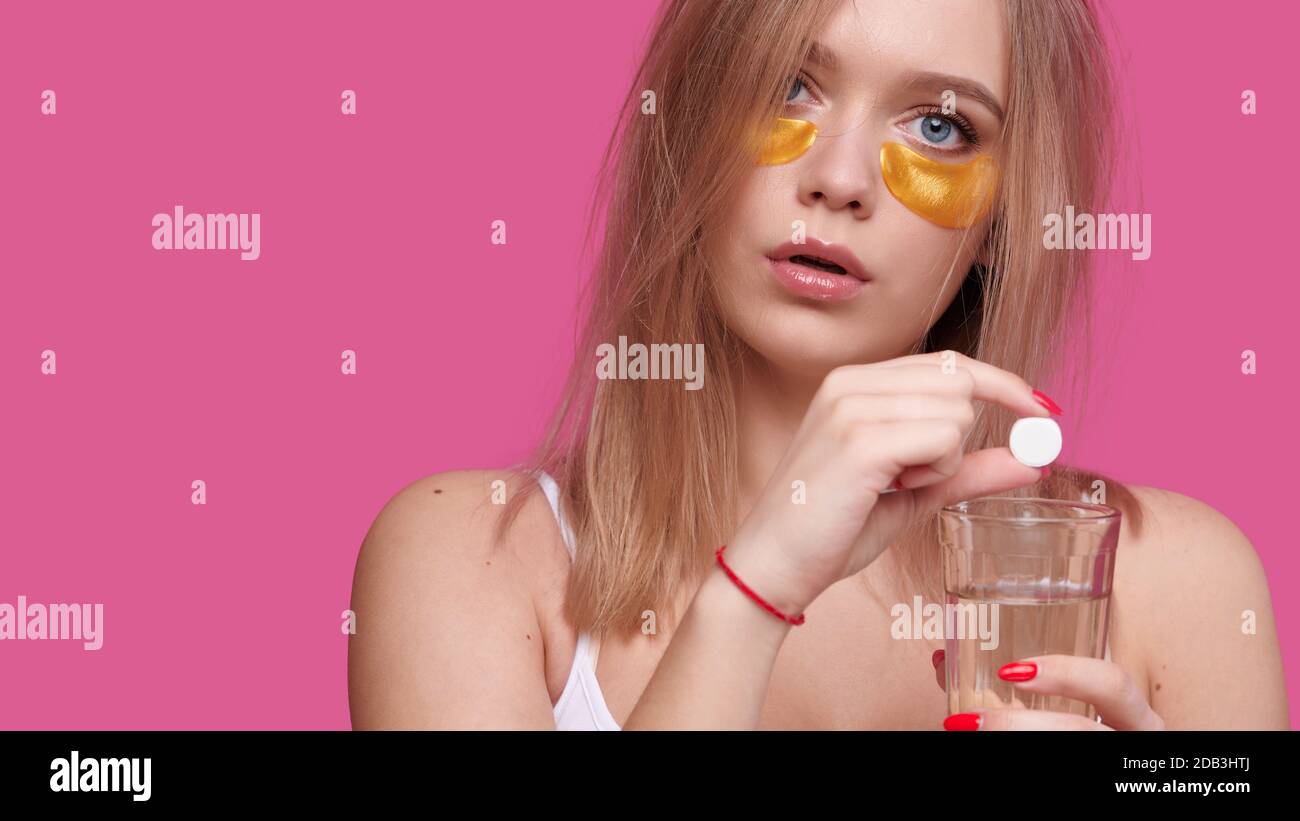 Woman with flowing hair puts pain reliever pill into glass of water after hangover on pink isolated background Stock Photo