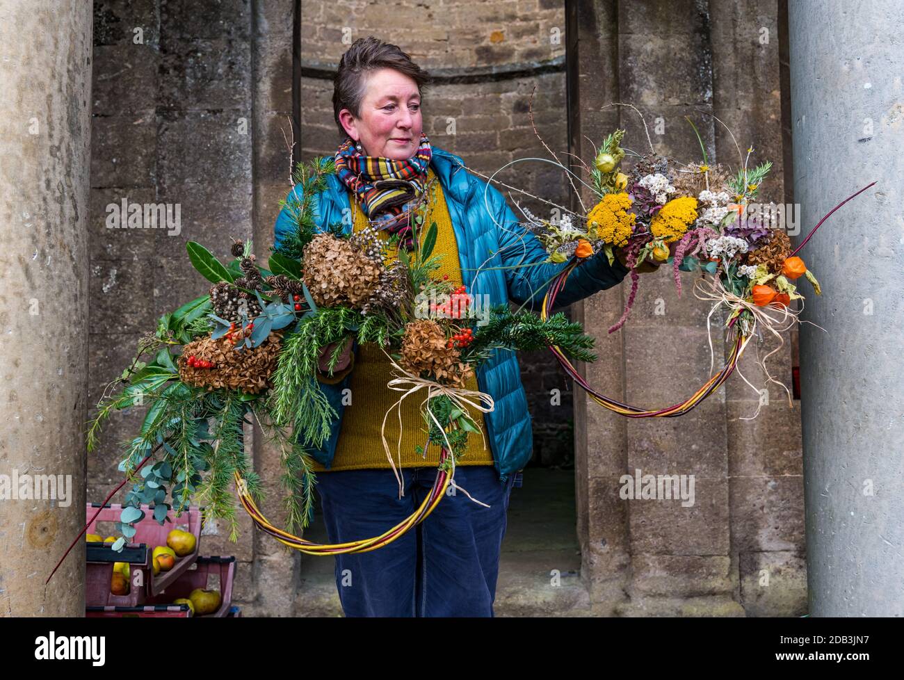 Haddington, East Lothian, Scotland, UK, Flowersmith prepares for Christmas:  Ruth Alder, a flower smith, weaves willow into wreaths to decorate for Christmas using foliage and flowers from Amisfield Walled Garden where she is a volunteer. Amisfield Walled garden is an 18th century garden managed by the Amisfield Preservation Trust and is free to visit all year round. Pictured: Ruth with finished Christmas decorated wreaths Stock Photo
