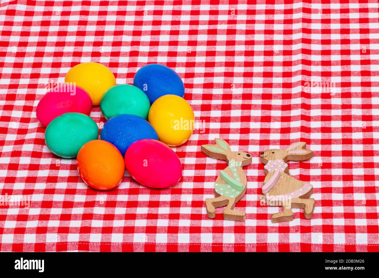 Happy Easter greeting card template. Top view of colorful eggs  and two wooden bunnies on a red checkered tablecloth. Large space for text. Religion a Stock Photo
