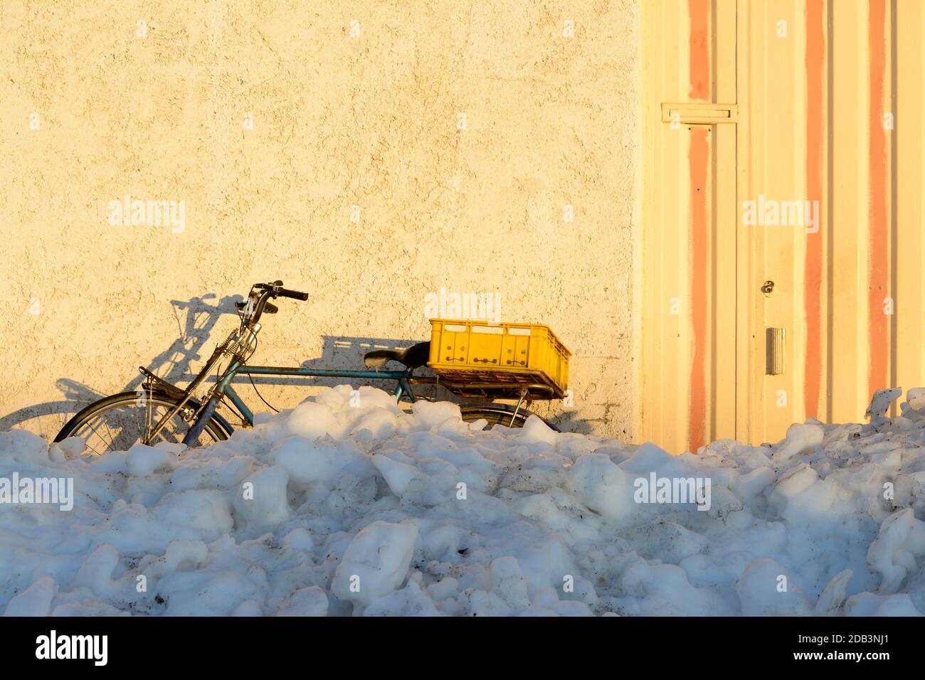 An antique bike with an empty yellow pot parked behind piled snow at street, city life Stock Photo