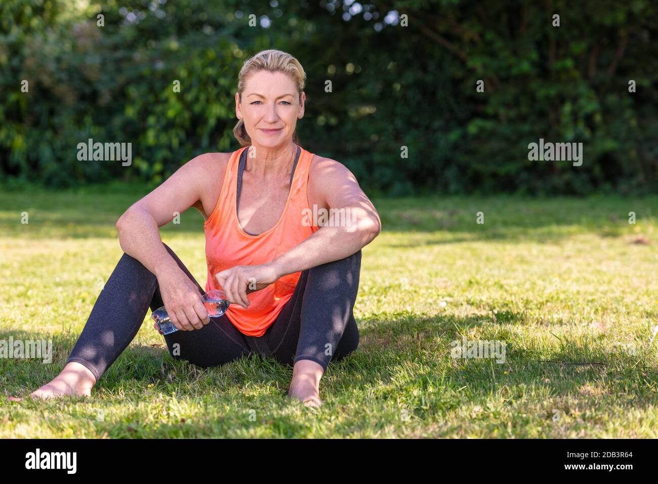 Outdoor portrait of an attractive middle aged blonde woman smiling drinking water relaxing after yoga, exercising, running or fitness lifestyle Stock Photo